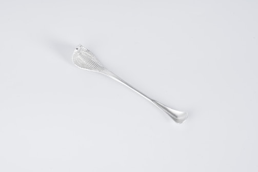 A sleek, metallic utensil with a textured handle. The design is minimalist, with a smooth, reflective surface and elegant curves.
