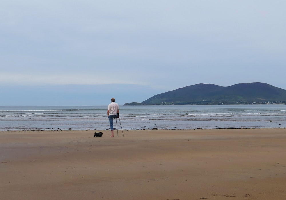 um homem em pé no topo de uma praia de areia ao lado do oceano