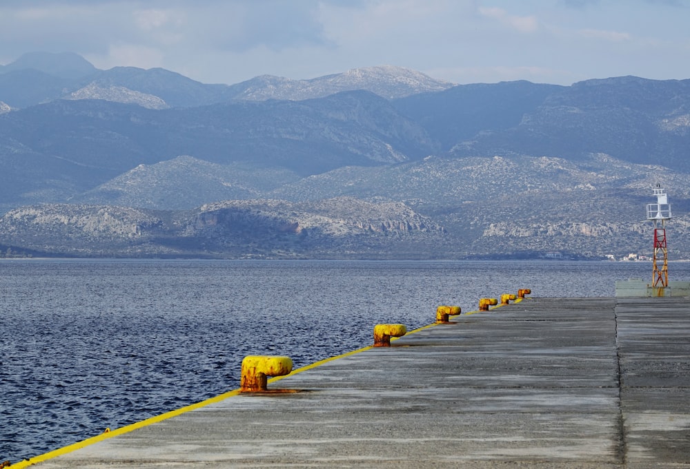 a pier with yellow buoys on the water and mountains in the background
