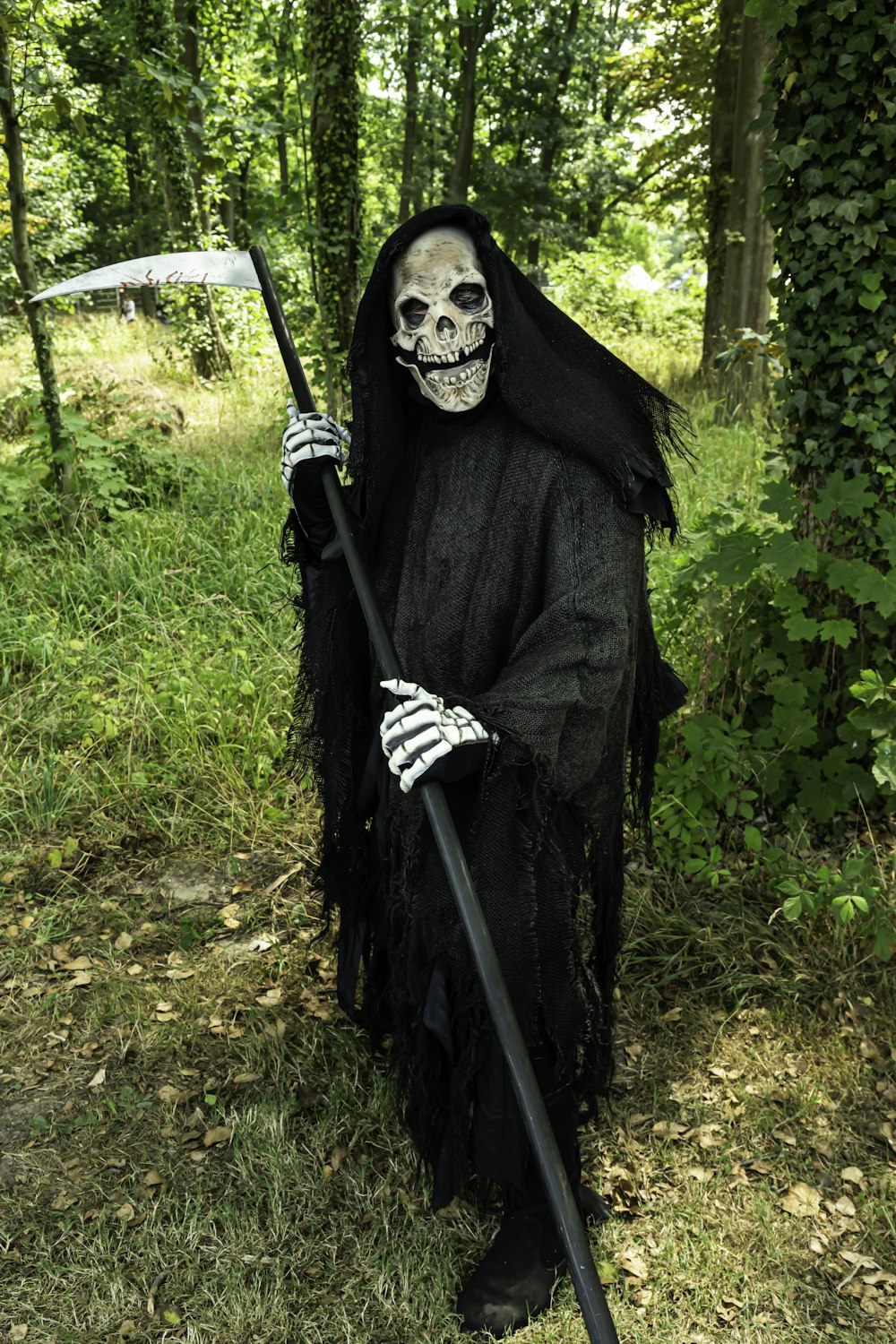 um esqueleto vestido com um manto preto e segurando uma vara longa