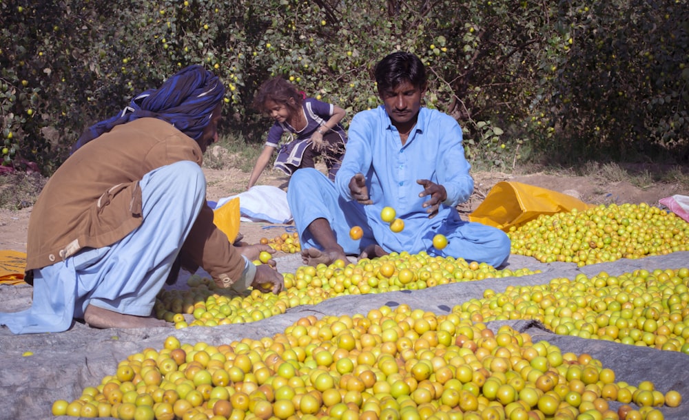 a group of people sitting around a pile of fruit