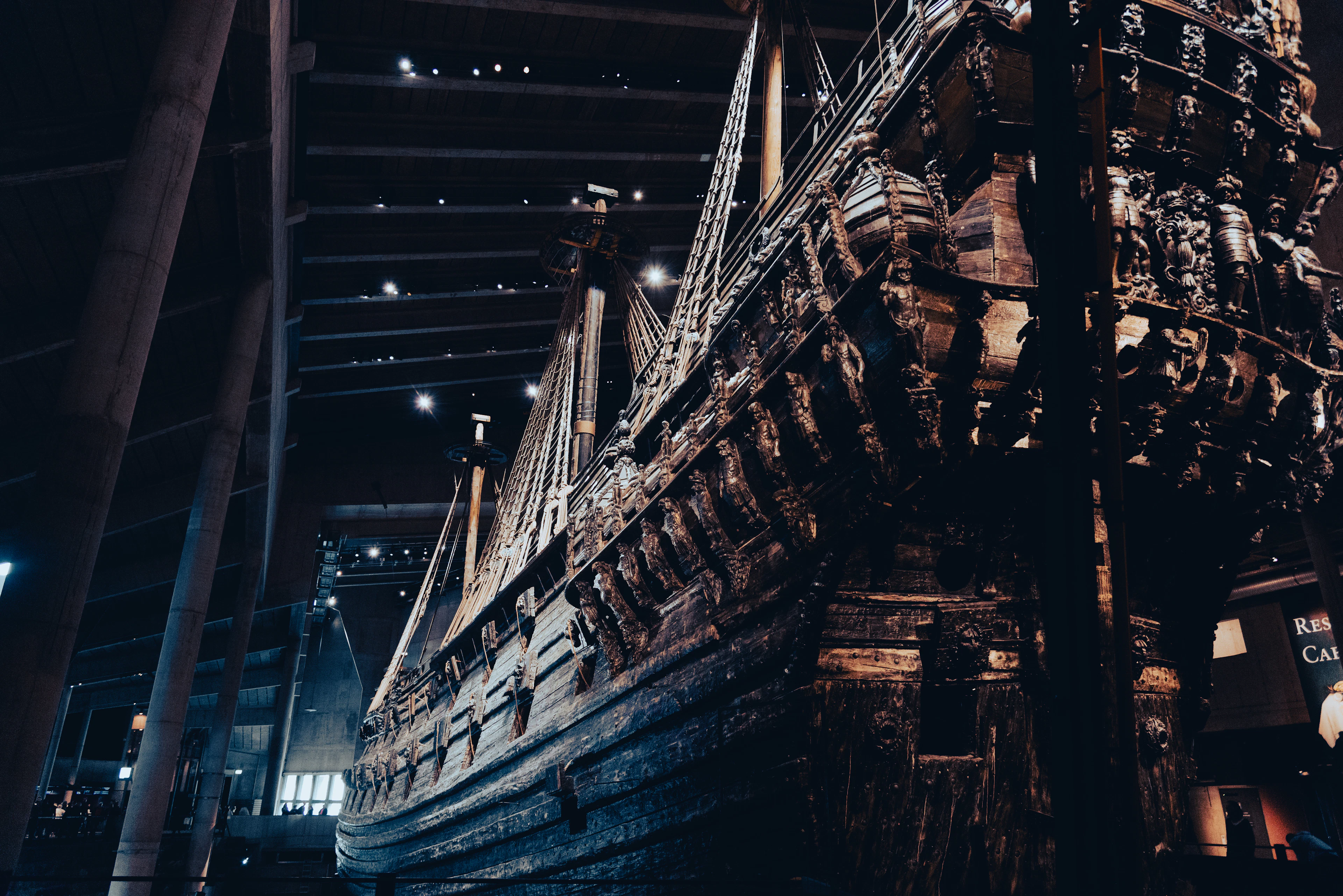 The salvaged 17th-century warship Vasa towering inside the darkened hall of the Vasa Museum in Stockholm, its carved stern and rigging lit warm against black timber walls.