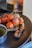 A grilled piece of meat is adorned with a cluster of vine-ripened cherry tomatoes on a black plate. A small dish with a greenish sauce accompanies the dish, and the focus is on the rich texture of the steak and glossy tomatoes. The background is softly blurred, lending a gourmet appeal.