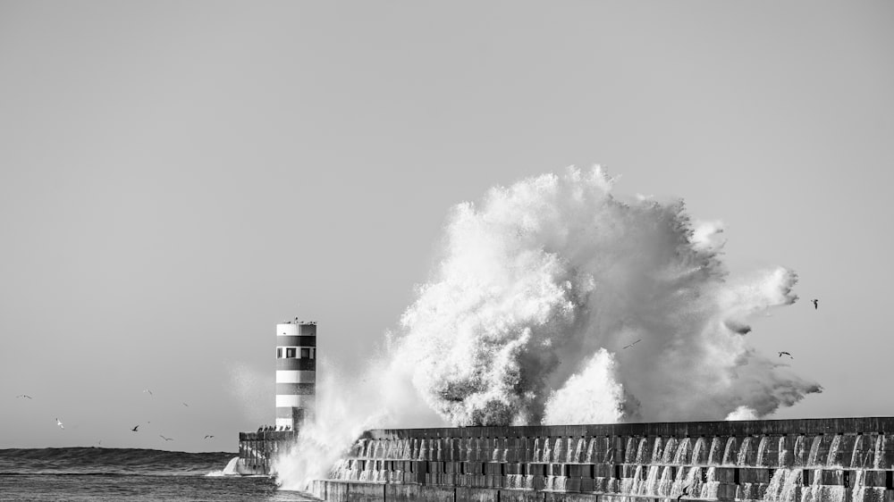 a black and white photo of a large wave hitting a lighthouse