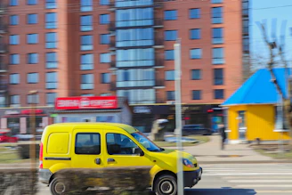 A bright yellow delivery van speeding along a highway under a clear blue sky.