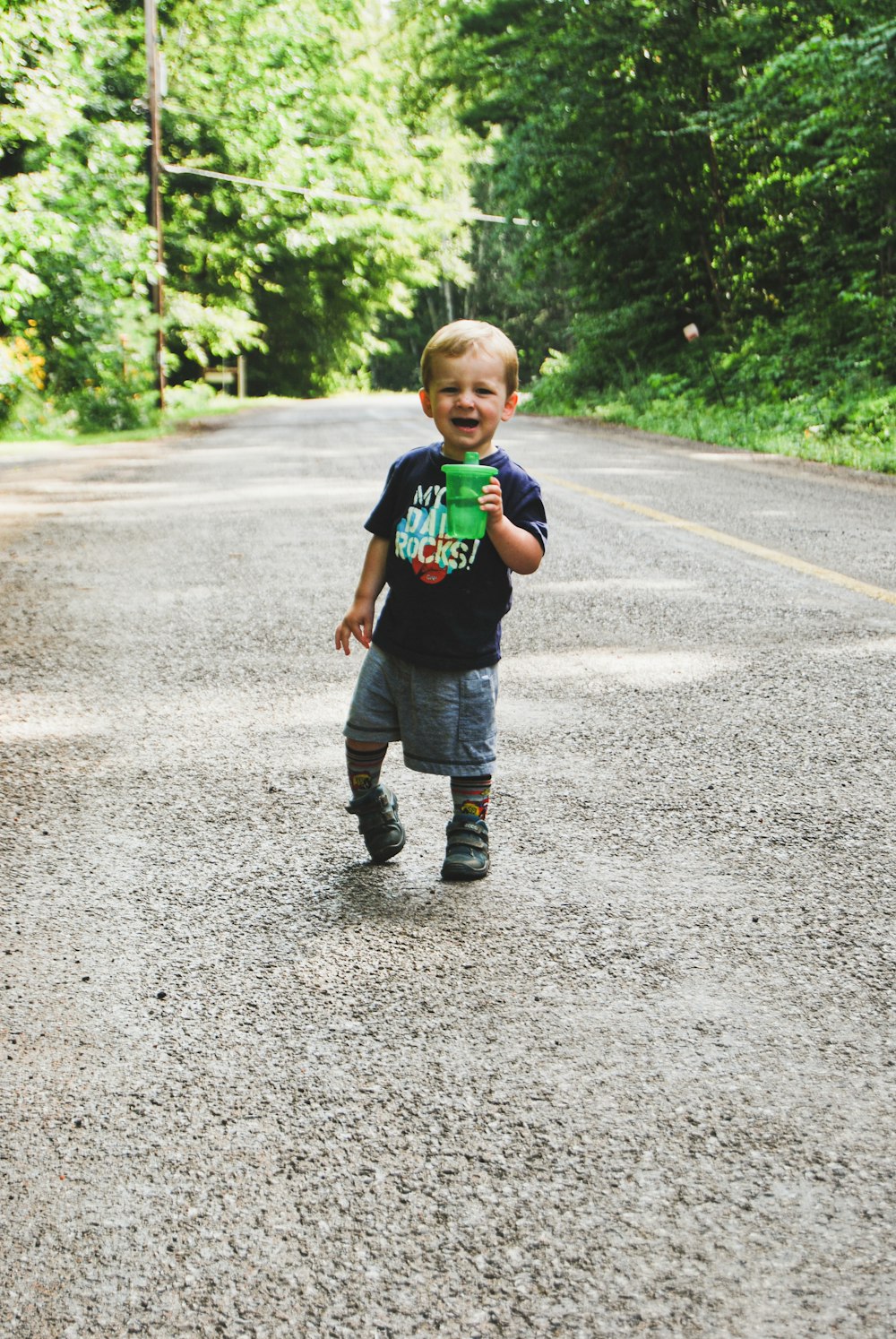 a young boy walking down a road in the middle of a forest