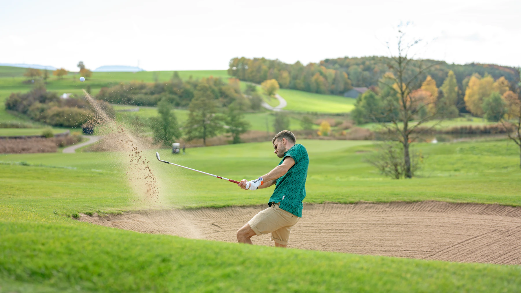 Golfer playing from a sand bunker on uneven ground.