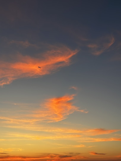 A sleek airplane soaring above fluffy white clouds during a vibrant sunset.