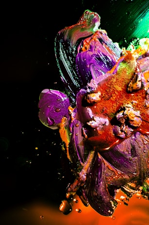 Vibrant strokes of paint blend together in an abstract composition featuring vivid purples, oranges, and greens. Thick applications of paint create texture and depth, with interspersed splashes and droplets adding dynamic movement.