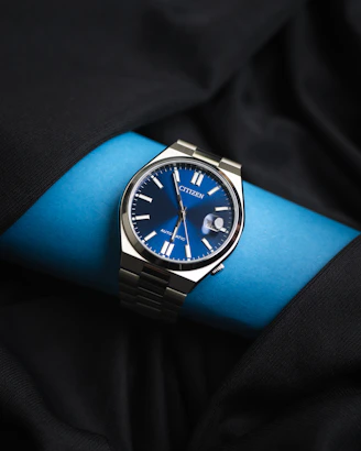 Close-up of a sleek men's watch with a deep blue dial and silver casing resting on a wooden table.