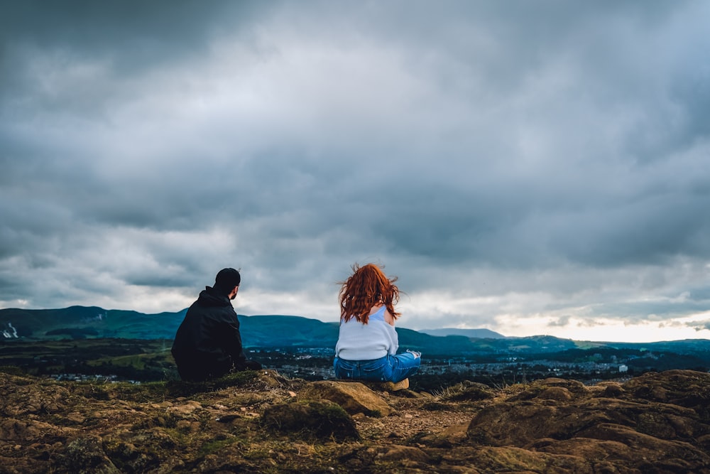 a man and a woman sitting on top of a hill