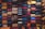 A variety of colorful bags are densely stacked against a wall, forming an organized display. Each bag comes in different shapes and textures, showcasing a wide range of materials such as leather and fabric. The bags are arranged in columns and rows, creating a visually striking pattern.