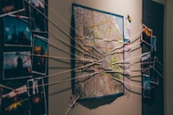 A wall display featuring a map in the center with strings connecting various photographs on either side, suggesting an investigative or planning scenario.