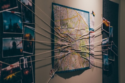 A wall display featuring a map in the center with strings connecting various photographs on either side, suggesting an investigative or planning scenario.