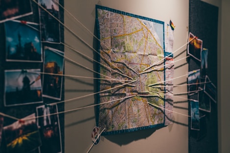 A wall display featuring a map in the center with strings connecting various photographs on either side, suggesting an investigative or planning scenario.