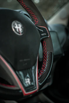 Close-up of a carbon fiber steering wheel with racing red stitching under dramatic lighting.