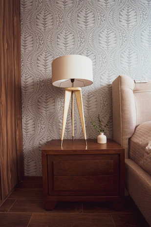 A bedroom corner featuring a wooden bedside table with a small plant and warm lighting.