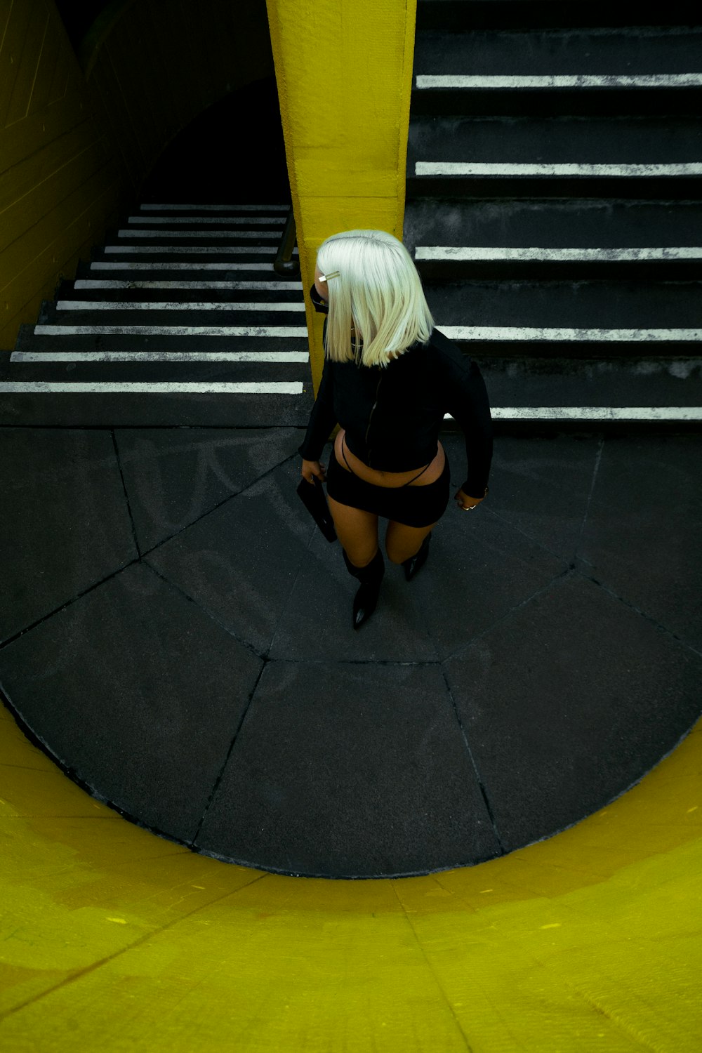 a woman in a black top is standing in front of a yellow wall