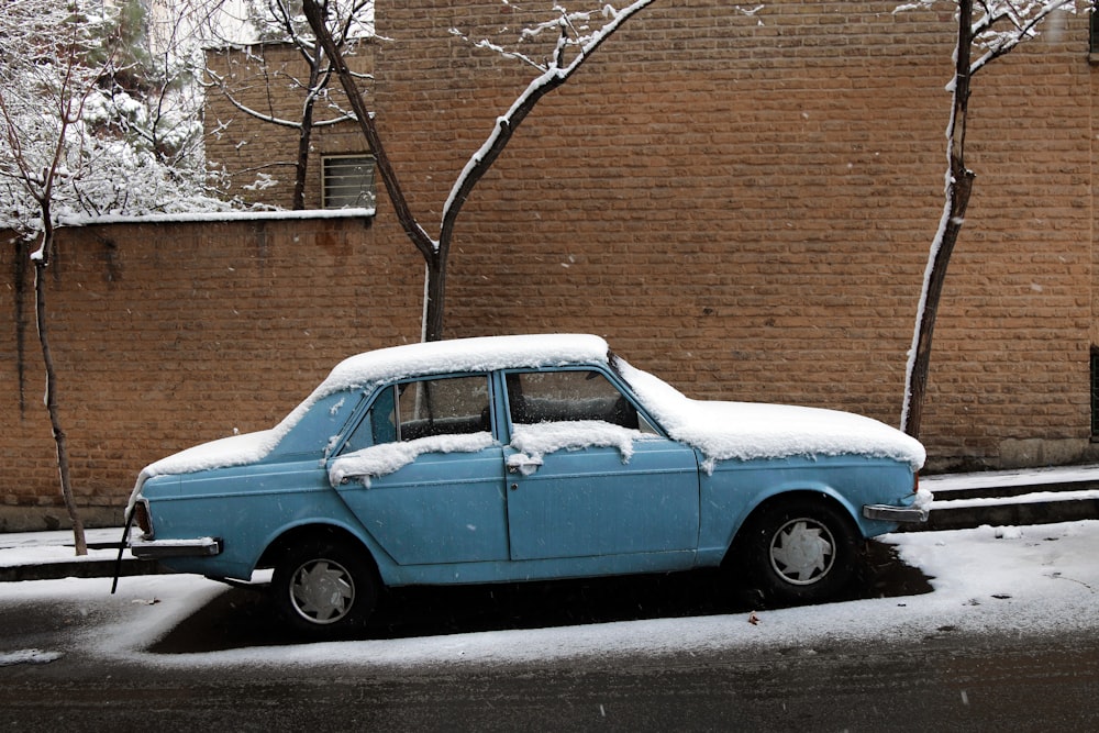 a blue car parked on the side of the road covered in snow