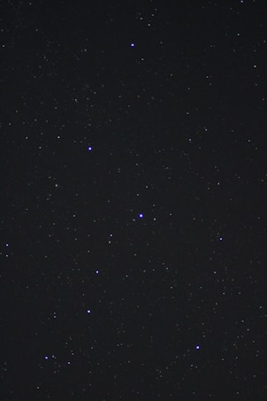 A dark night sky filled with numerous small stars scattered across the frame. Some stars appear brighter and larger than others, creating a sparkled effect against the black vastness of space.