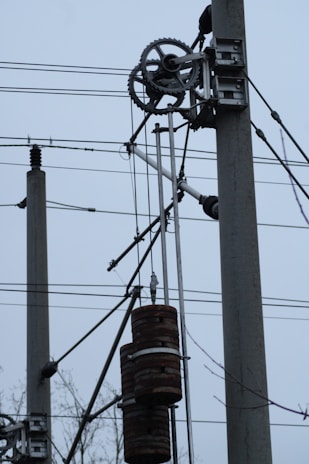 Electrical utility poles with wires and gears are visible. The setup includes weights that may be part of an industrial mechanism or telecommunication infrastructure.