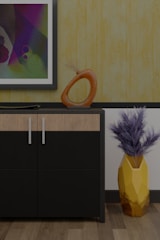 A modern interior scene featuring a cabinet with a sleek black and wood finish. On top of the cabinet, there is an abstract orange sculpture with a circular design and a flat decorative element. A framed abstract painting hangs on the wall above, displaying a variety of colors including purple, green, and blue. To the right of the cabinet, a geometric yellow vase holds dried branches, adding a touch of natural texture. The background features a textured yellow wallpaper, complementing the wooden floor.