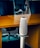 A modern office setting with sleek black office chairs around a wooden table. At the forefront, a tall, cylindrical speaker or device stands on a metallic stand.