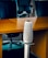 A modern office setting with sleek black office chairs around a wooden table. At the forefront, a tall, cylindrical speaker or device stands on a metallic stand.