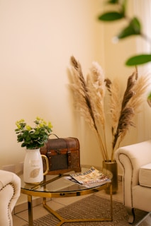 a living room with a glass table and a vase with flowers on it, tall vase with pampas grass