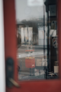 A gumball machine filled with colorful gumballs is visible through a glass door. The scene is an indoor setting with some blurred and indistinct objects and papers on shelves in the background.