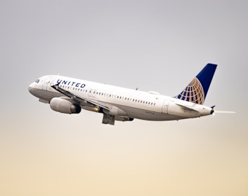 A commercial airplane with white and blue colors is flying in the sky. The aircraft bears the United Airlines logo and has a sleek, modern design with engines visible under the wings.