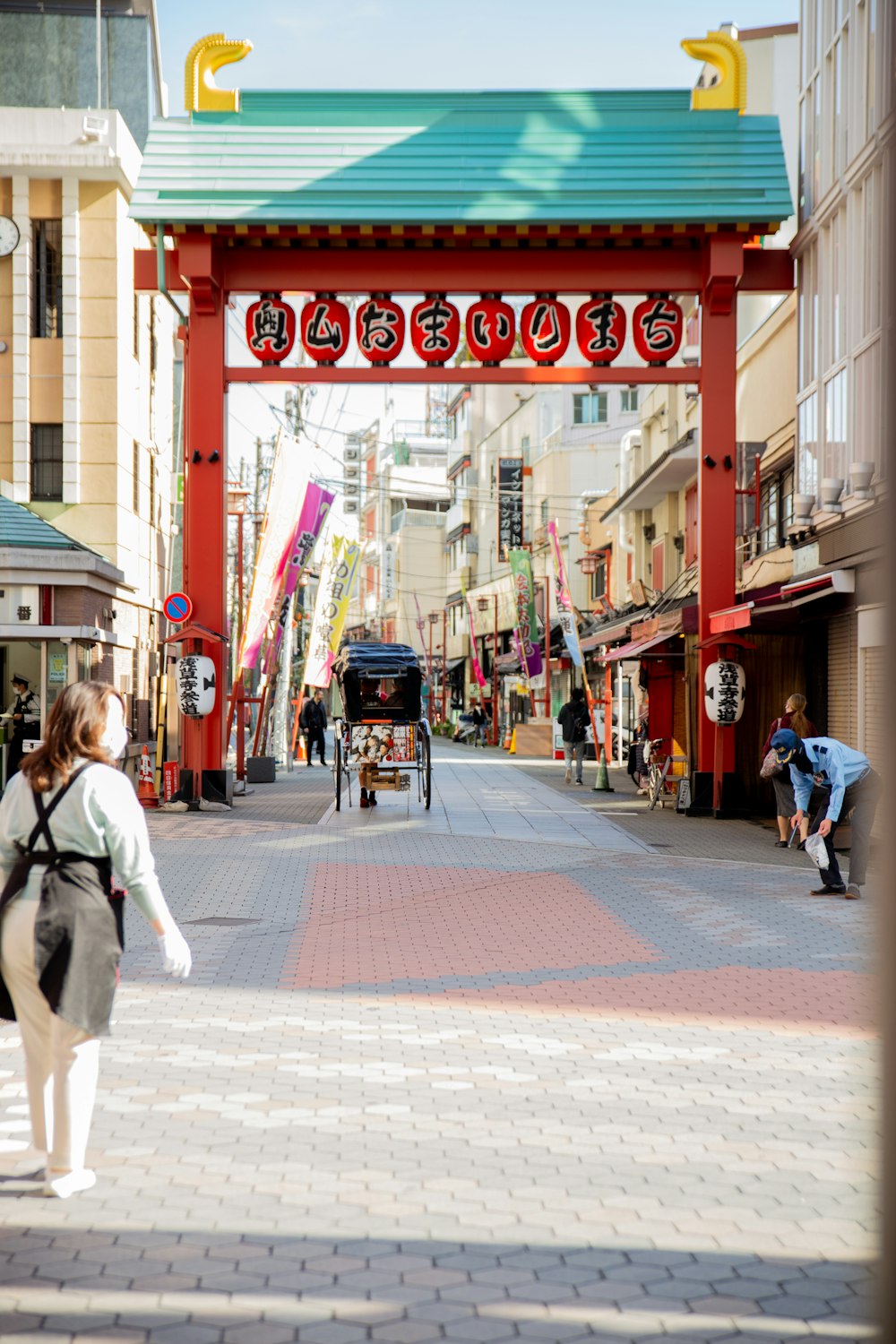 a woman walking down a street under a red arch