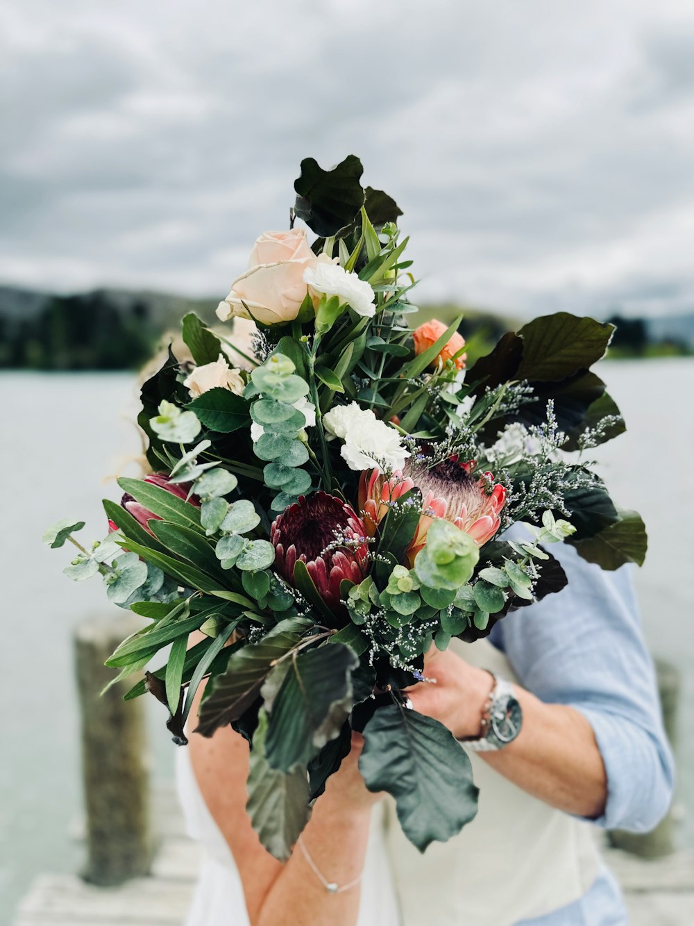 a woman holding a bouquet of flowers near a body of water