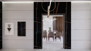 A modern interior features a sleek, minimalist design with a large doorway leading into a dining area. The walls are adorned with black and white marble details, complemented by geometric artwork. The dining room has a wooden table surrounded by upholstered chairs, and a contemporary chandelier hangs overhead.