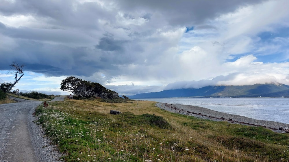 a dirt road next to a body of water under a cloudy sky