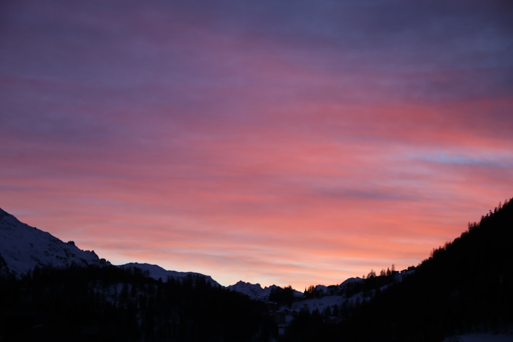 a sunset view of a mountain range with trees in the foreground