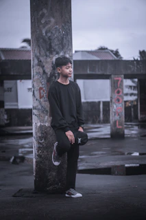 Model wearing a dark, edgy t-shirt standing against a weathered brick building at dusk.