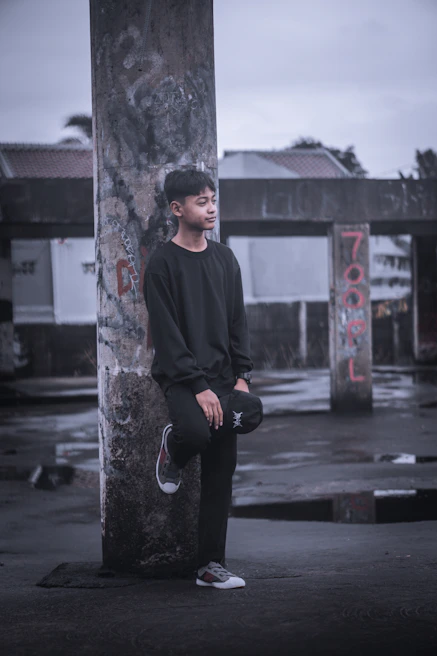 Model wearing a dark, edgy t-shirt standing against a weathered brick building at dusk.