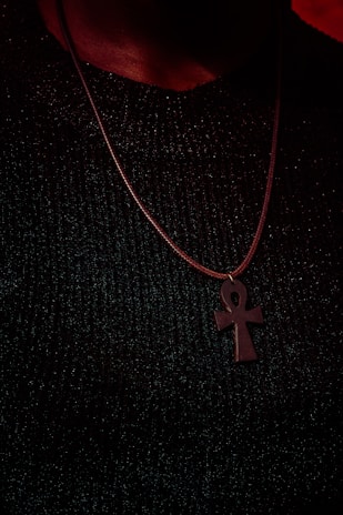 Close-up of a gleaming silver ankh pendant resting on rich, dark velvet fabric.