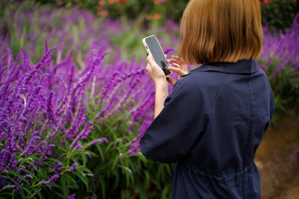 a woman standing in a field of purple flowers looking at a cell phone