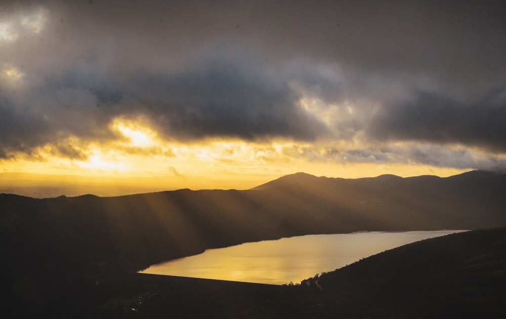 a lake surrounded by mountains under a cloudy sky