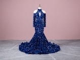 An elegant evening gown in deep blue, showcased on a mannequin in natural light.