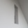 A minimalistic wall design with a rectangular cutout, revealing a glimpse of a staircase railing within a modern interior space characterized by clean lines and geometric shapes.