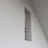 A minimalistic wall design with a rectangular cutout, revealing a glimpse of a staircase railing within a modern interior space characterized by clean lines and geometric shapes.