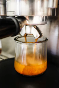Close-up of a barista carefully pouring espresso into a clear glass, highlighting rich crema and aroma.