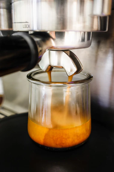 Close-up of a steaming espresso shot being pulled with rich crema on top.