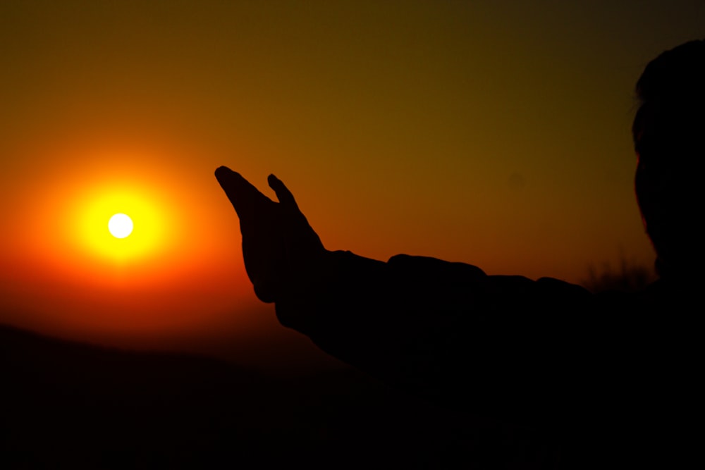 une personne levant la main vers le soleil