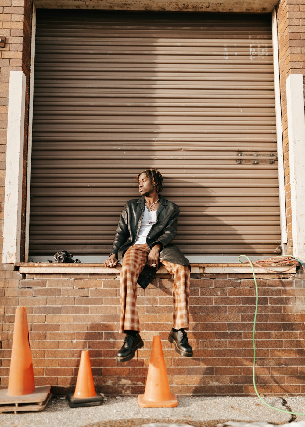 a man sitting on a window sill next to orange cones