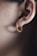 A close-up of a person's ear adorned with a hoop earring shaped like a snake. The earring is golden with a detailed, textured design resembling scales. The ear's outline is clearly visible, and the lighting highlights the smooth skin and the earring's metallic sheen.