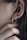 A close-up of an ear adorned with a gold, textured hoop earring resembling a coiled snake. Fingers gently touch the area near the earring, emphasizing the jewelry's intricate details and the texture of the skin.